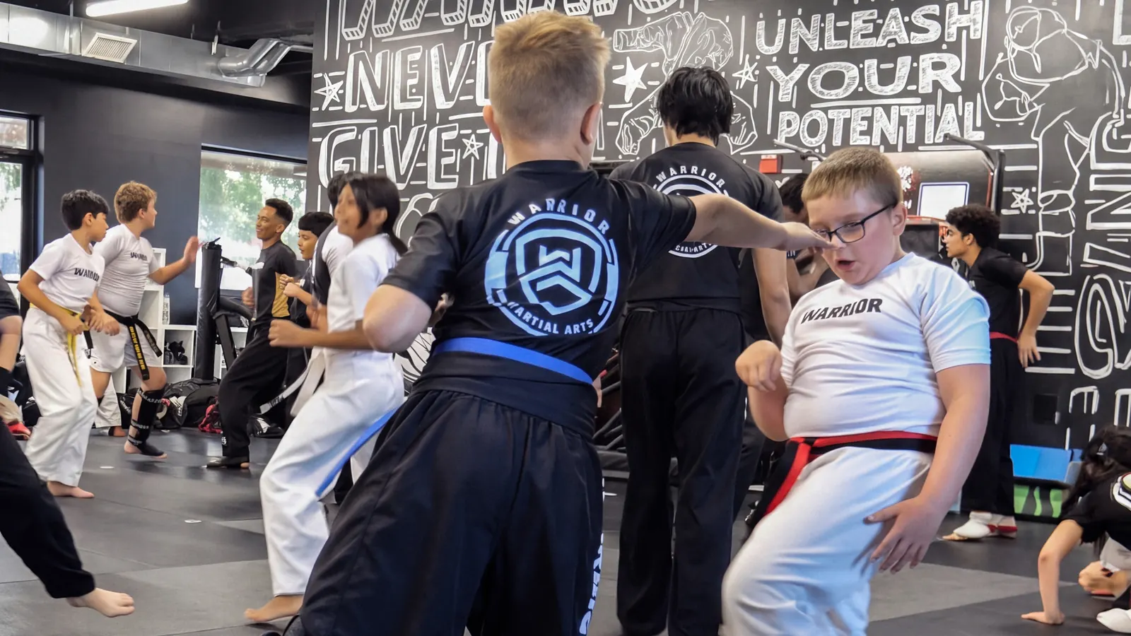 A Warrior student lands a kick during partner drills under the Never Give Up mural at the Dunellen studio