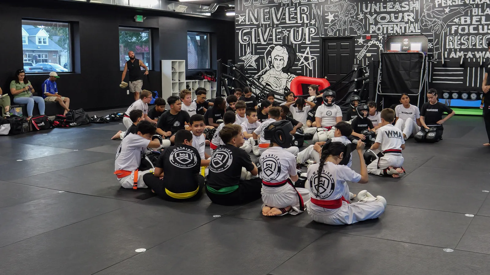 Warrior students seated on the mat listening to their coach at the end of class