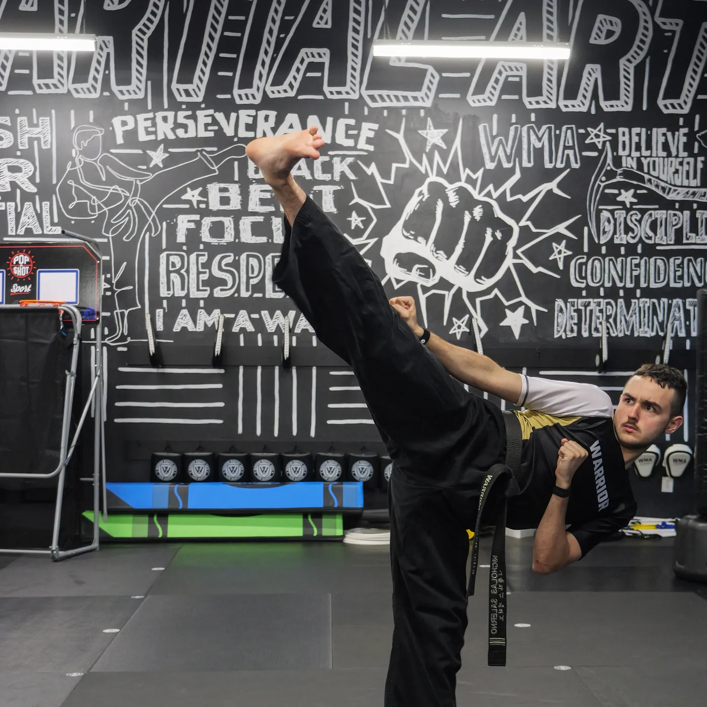 A Warrior head coach demonstrates a high kick in front of the studio wall art